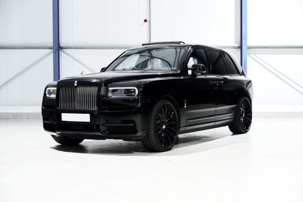 A black rolls-royce cullinan suv parked inside a white industrial building, featuring a glossy finish and dark-tinted windows.