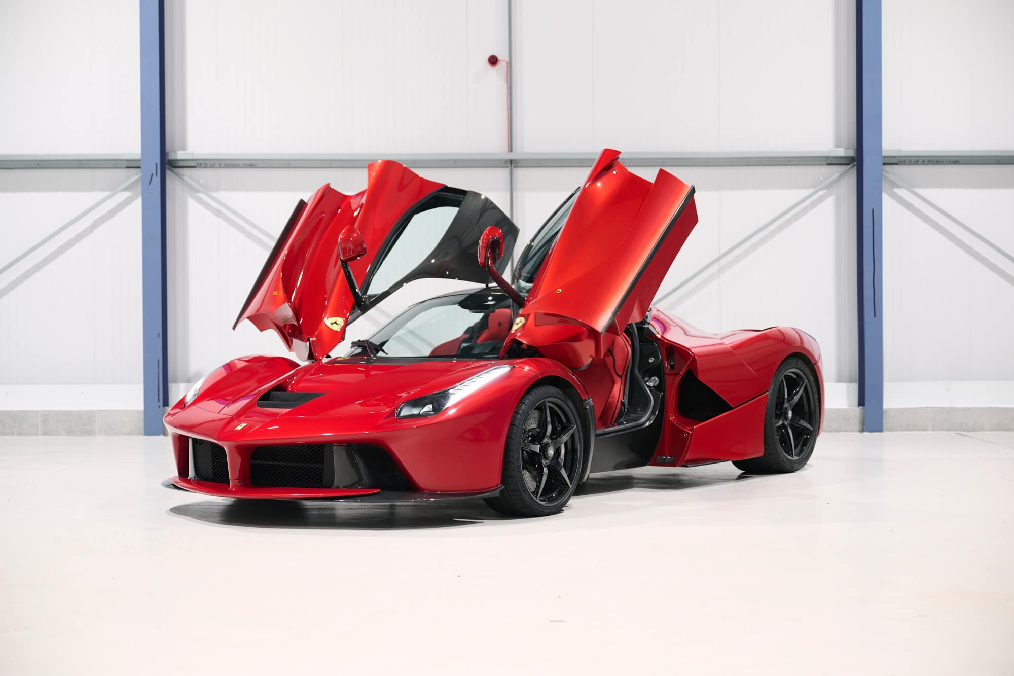 Red sports car with upward-opening doors in an indoor setting, showcasing a sleek and modern design.