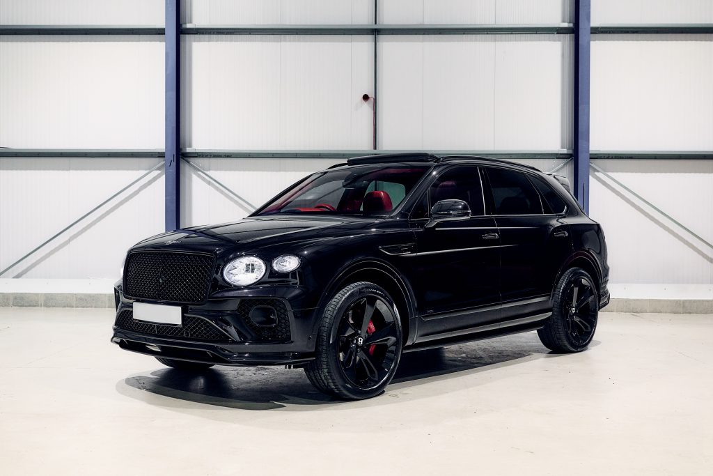 A black luxury SUV is parked in an indoor setting with a white and grey background. The vehicle, available for hire, features black rims and red interior accents.