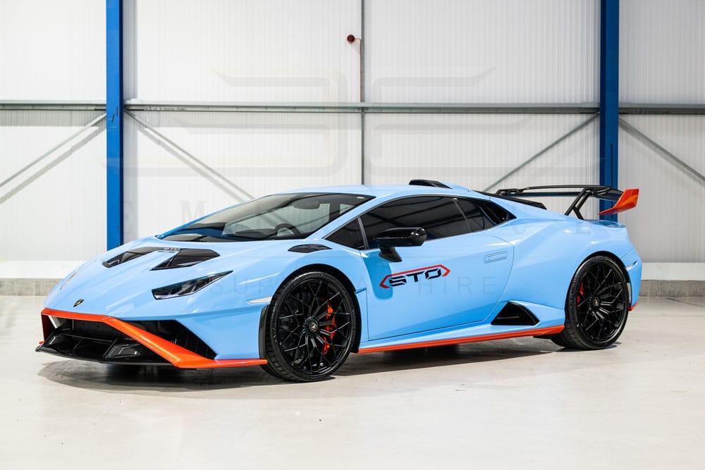 Blue lamborghini huracan sto parked in a warehouse, featuring a prominent rear spoiler and orange accents.