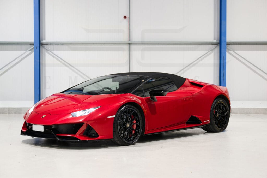 A red lamborghini huracan spyder parked in a clean, white industrial garage.
