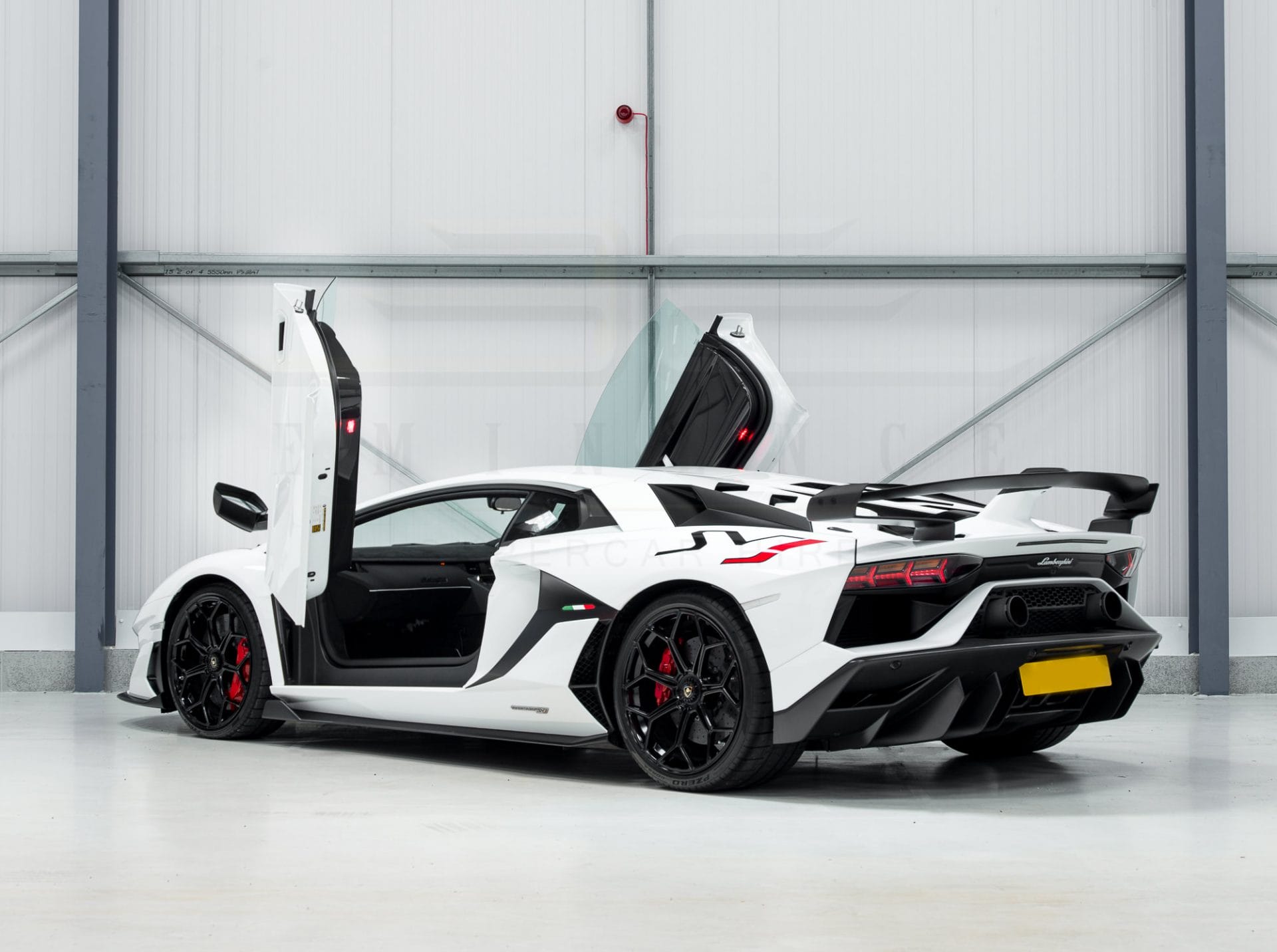 White lamborghini aventador with doors open, parked in a modern garage with a clean, grey background.