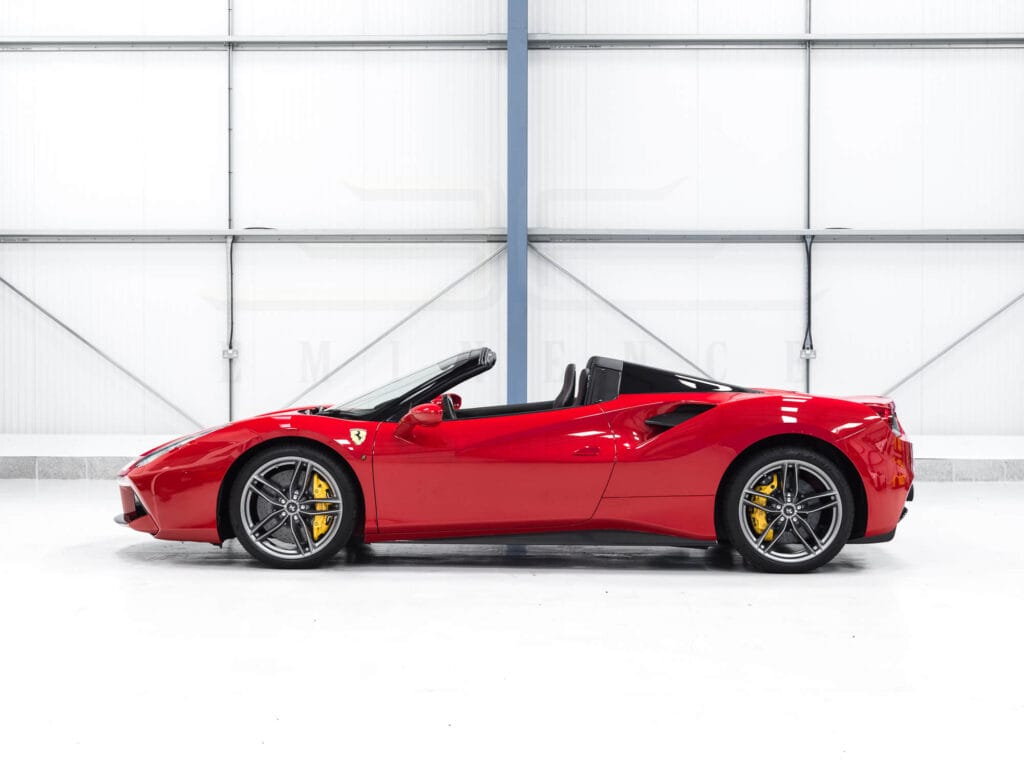 Red ferrari 488 spider convertible parked in a white showroom.