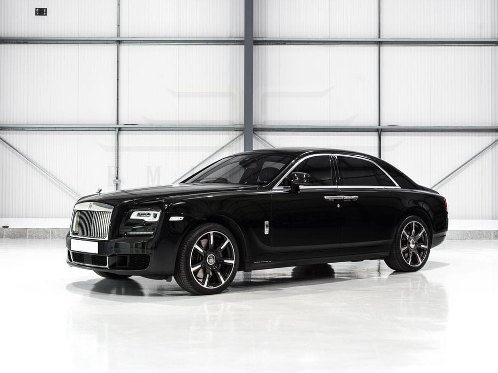A black rolls-royce ghost parked inside a brightly lit, white industrial garage.