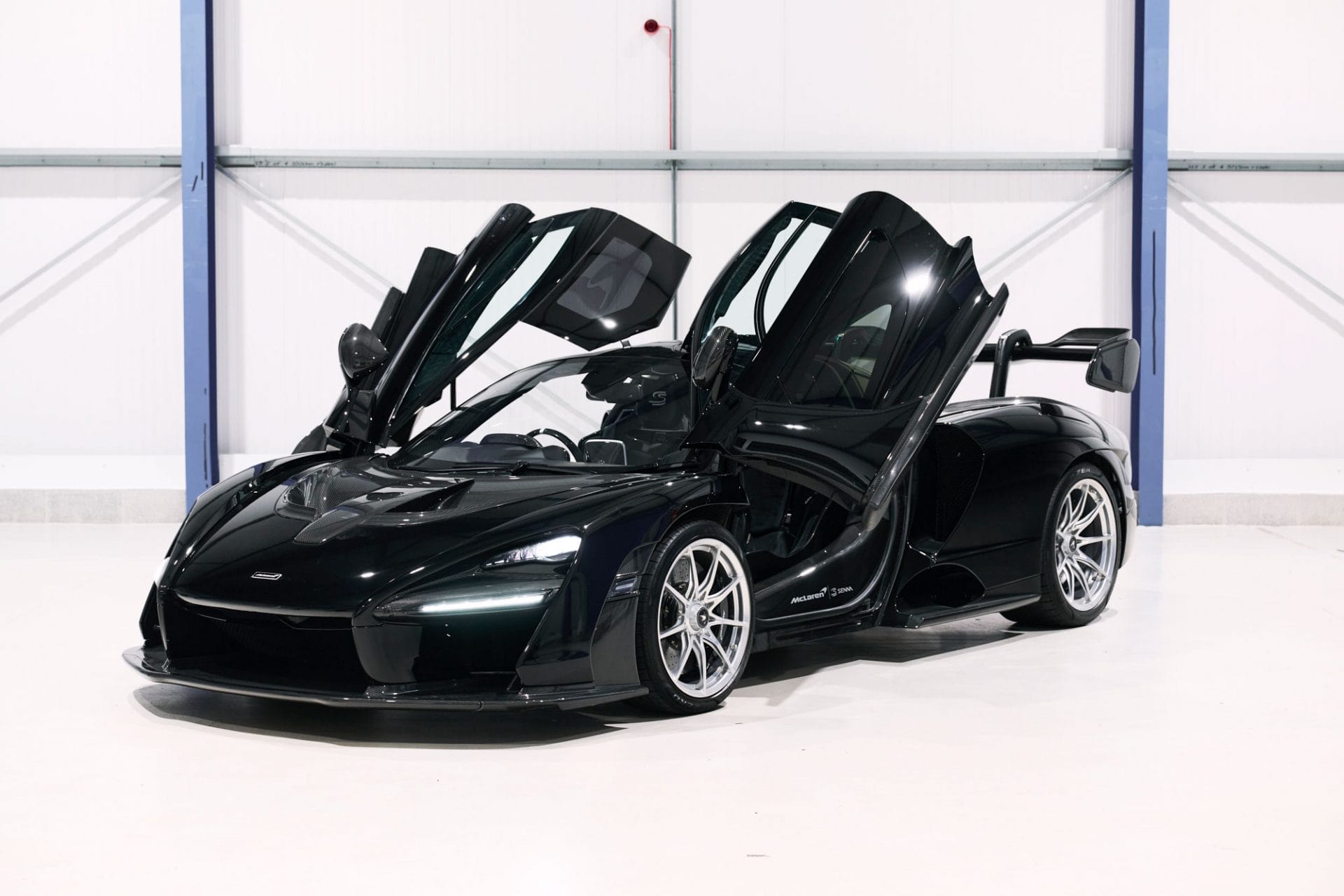 A black mclaren sports car with open butterfly doors parked inside a showroom.
