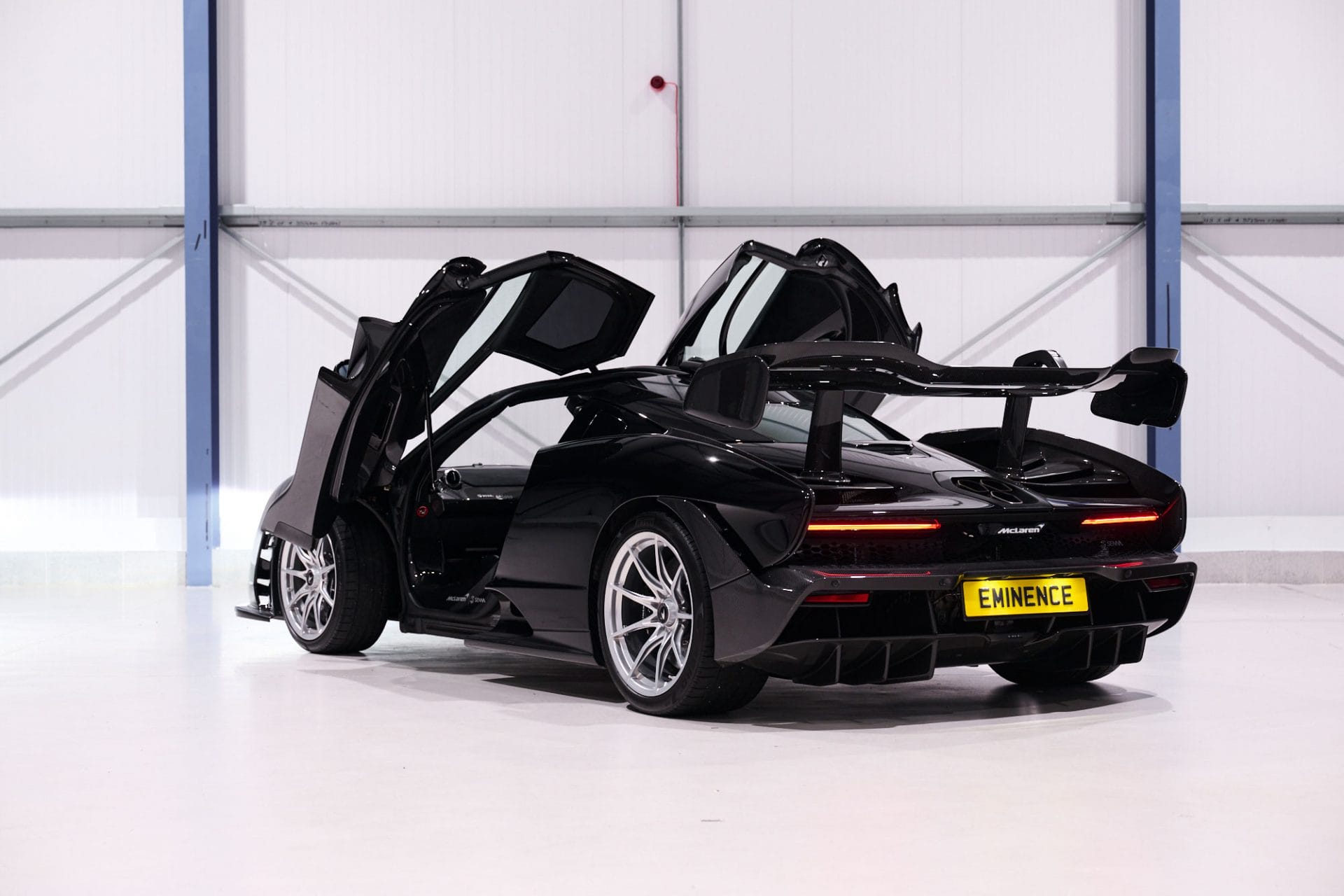 Black sports car with open butterfly doors and rear spoiler inside a white showroom.