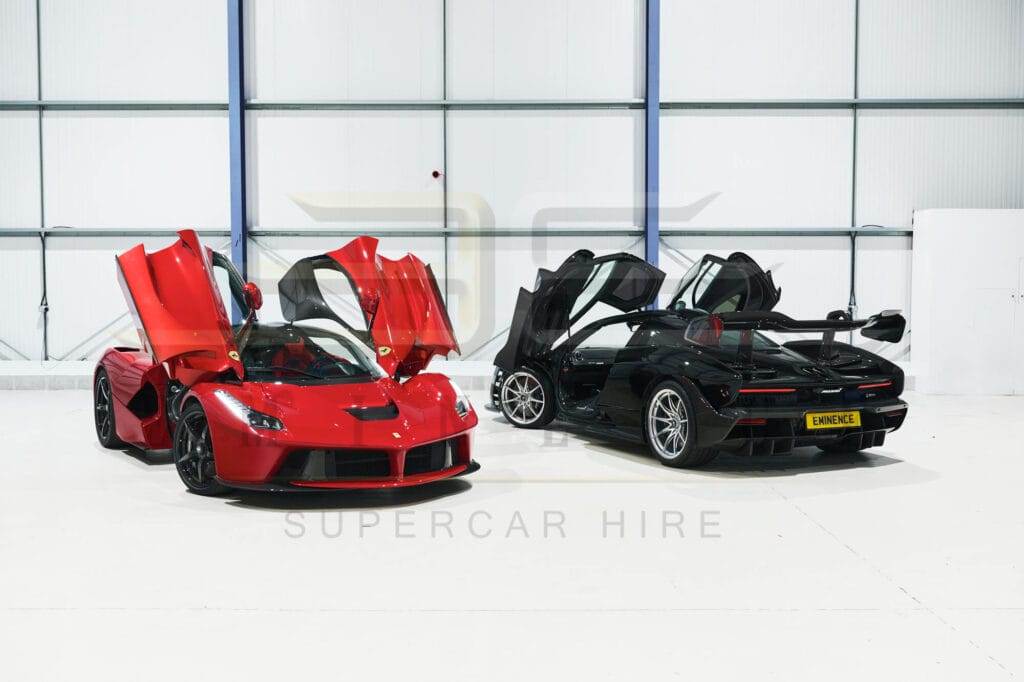 Two sports cars with butterfly doors open are displayed in a pristine white indoor setting. The car on the left is red, and the car on the right is black, both available for hire to those seeking a thrilling ride.