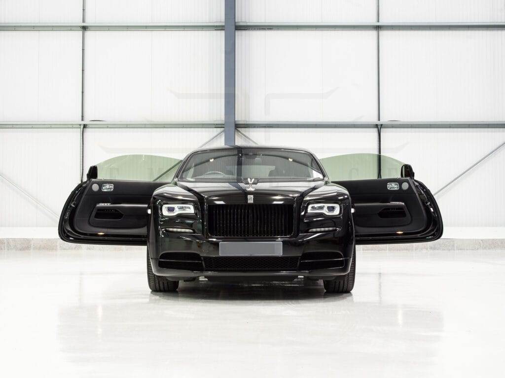 Front view of a black luxury car with butterfly doors open, available for hire, displayed in a well-lit indoor showroom.