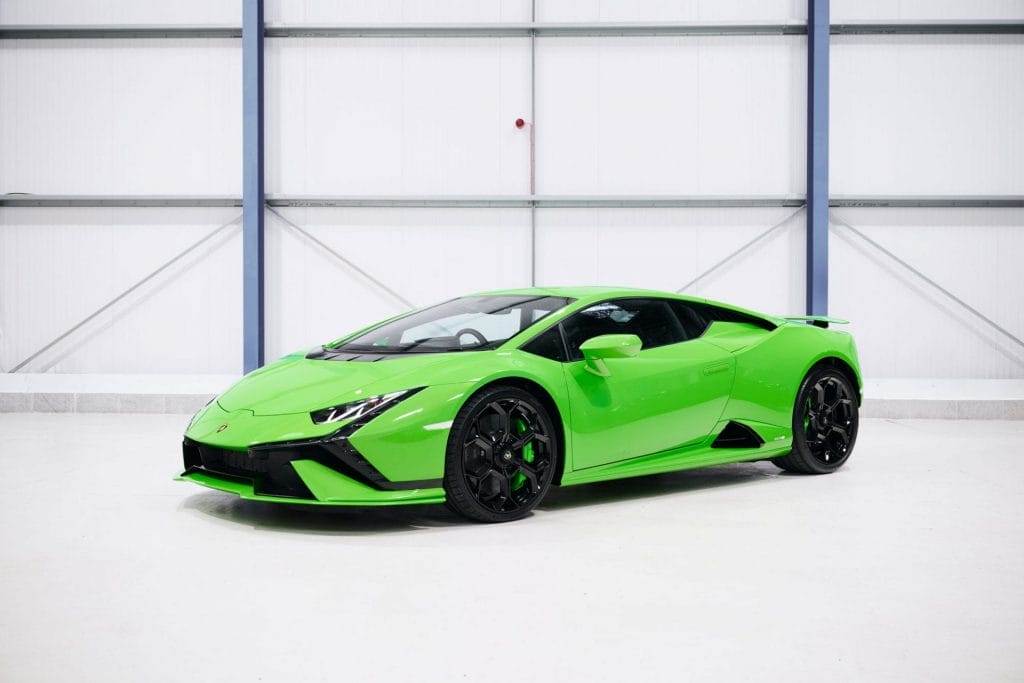 A bright green sports car, available for hire, is parked in a large, clean, industrial-looking indoor space with white walls and a high ceiling.